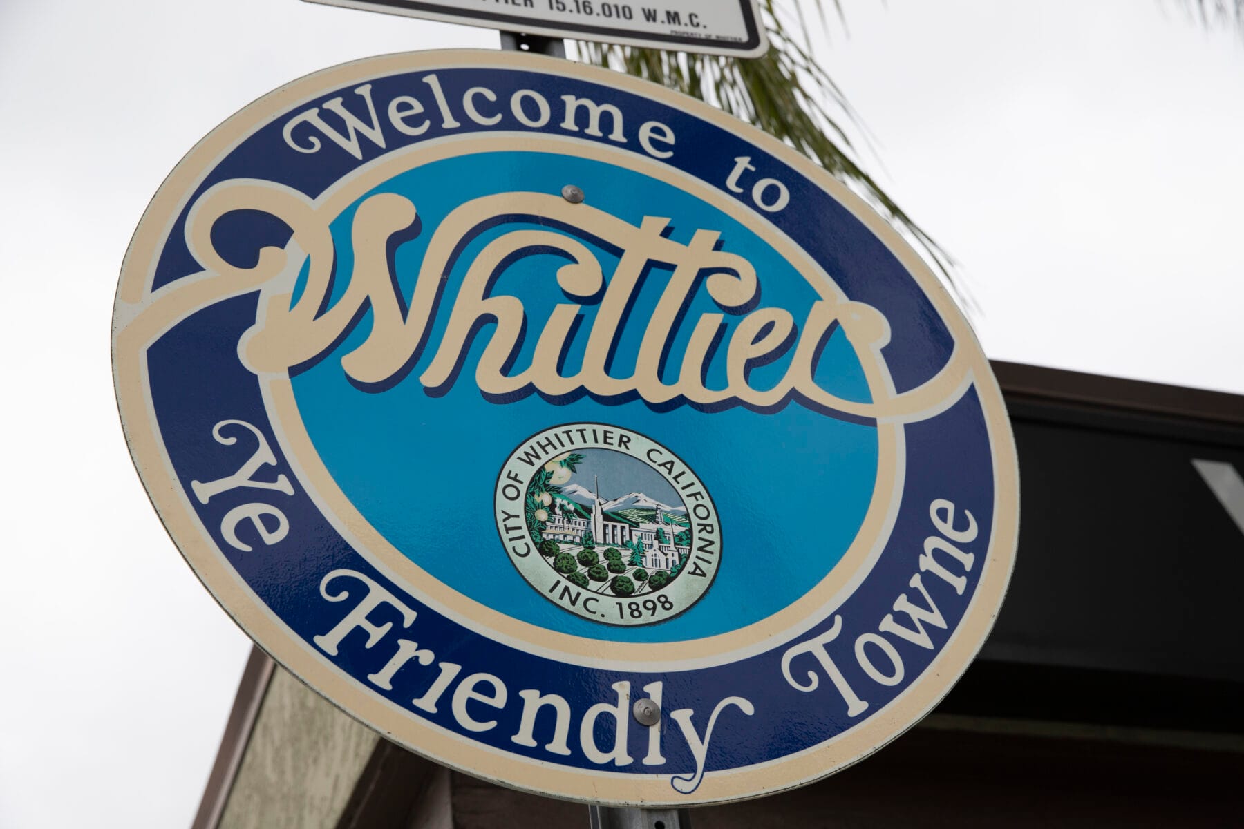 a blue and white sign reading 'Welcome to Whittier, Ye Friendly Towne' with the city seal in the center